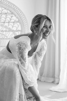 a woman in a white dress is sitting on a chair and smiling at the camera