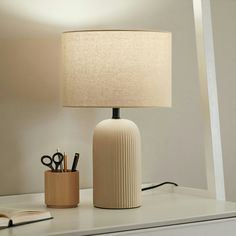 a table lamp sitting on top of a desk next to a cup and pen holder