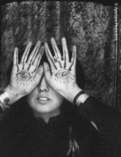 a woman holding her hands up to her face with all seeing eyes painted on it