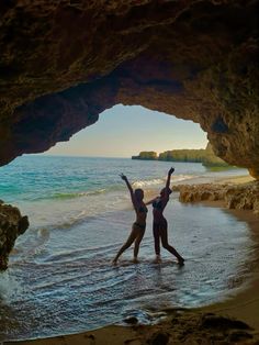 two people are standing in the water at the beach with their hands up and arms raised