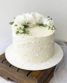 a white wedding cake with flowers on top sits on a wooden box and is ready to be cut