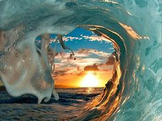 an ocean wave with the sun setting in the background and some water swirling around it