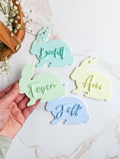 someone holding up some bunny shaped magnets with the word easter written on them in blue, green and white