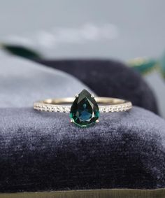 a ring with a large green stone on it sitting on top of a velvet cushion