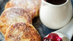 powdered sugar and jelly pastries on a plate next to a cup of coffee