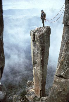 a man standing on top of a large rock next to a cliff in the sky