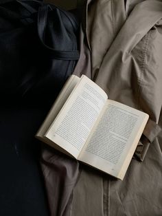 an open book sitting on top of a bed next to a black bag