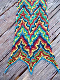 a multicolored crocheted scarf on a wooden floor next to a piece of wood