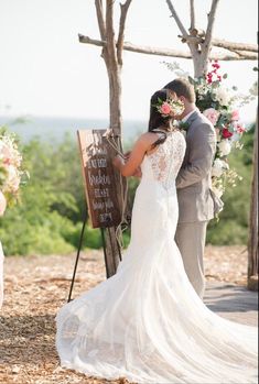 a bride and groom kissing under a wooden sign at their outdoor wedding in the woods