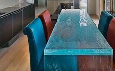 a long table with blue and red chairs in a kitchen next to a stove top oven