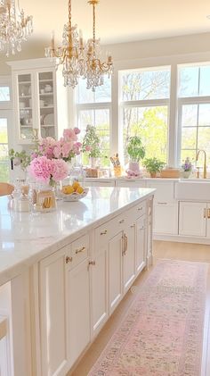 a large kitchen with white cabinets and pink flowers in the center island, along with chandeliers