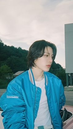 a man in a blue jacket leaning on the hood of a car