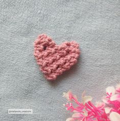 a pink crocheted heart sitting on top of a blue towel next to flowers