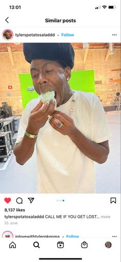 a man eating food while wearing a white t - shirt and black cap on his head