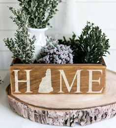 a wooden sign with the word home on it sitting next to some flowers and greenery