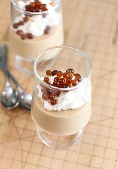 two glasses filled with dessert sitting on top of a wooden table next to spoons