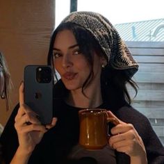 two women holding up their cell phones and coffee mugs while looking at the camera