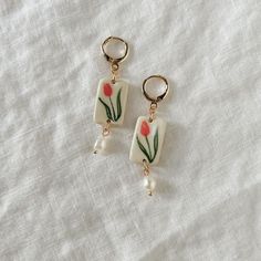 two earrings with flowers and pearls hanging from them on a white cloth covered tablecloth