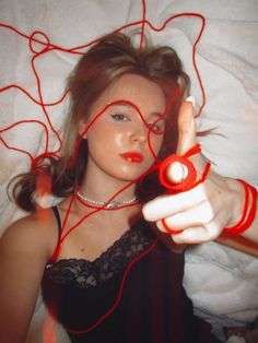 a woman laying in bed with red thread on her head and fingers pointing at the camera