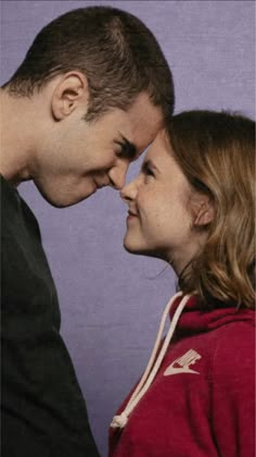 a man and woman standing next to each other in front of a purple wall together