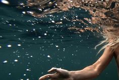 a woman is swimming in the ocean with her hands out to touch the water's surface