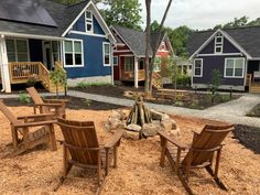 a fire pit surrounded by wooden chairs in front of some small blue houses and trees