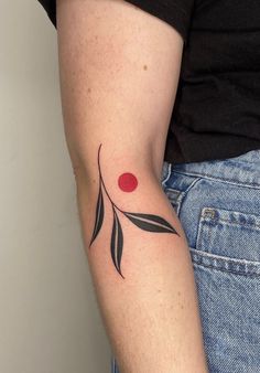 a woman's arm with a tattoo on it that has leaves and a red dot