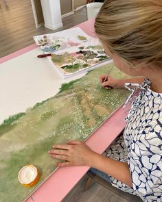 a woman sitting at a table working on an art project with watercolors and paper