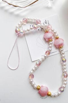 a bracelet with pearls and seashells on it next to a white card holder