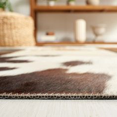 a brown and white cowhide rug on the floor in front of a wooden shelf