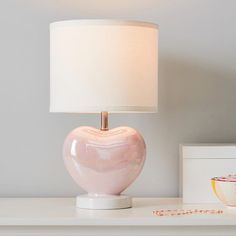 a pink heart shaped lamp sitting on top of a white table next to a bowl