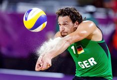 a man is hitting a ball with his racket in the air while wearing a green shirt