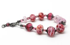 "In the mood for pink? Then this bracelet fits perfectly! It features a selection of my handmade pink lampwork beads. The colors range from dark translucent pink, pink and purple frit beads, to light pink swirls. These beads are simply stunning! Such a beautiful combination for Spring! The beads are strung along side sterling silver flower bead caps and pink Tourmaline rectangle shaped gemstone beads. I have made the lampwork beads in this bracelet. The sterling silver has been oxidized to add d Pink Beaded Bracelets With Spacer Beads As Gift, Adjustable Pink Glass Bracelets, Pink Bracelets With Large Beads For Jewelry Making, Adjustable Pink Bracelets, Pink Glass Beaded Bracelets As Gift, Handmade Pink Glass Bracelets, Pink Czech Glass Beaded Bracelets With Colorful Beads, Pink Czech Glass Bracelets With Spacer Beads, Pink Czech Glass Beaded Bracelet With Colorful Beads