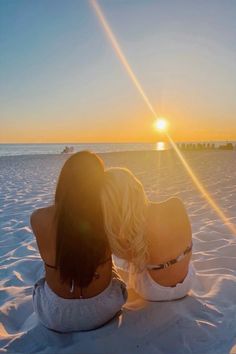 two women sitting in the sand watching the sun go down