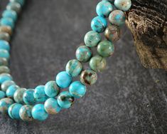 two strands of turquoise and brown beads on a tree branch with a piece of wood in the background