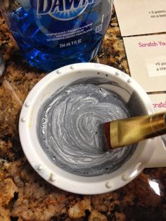 a bottle of water sitting next to a bowl of silver colored paint and a brush