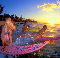 three girls on surfboards in the ocean at sunset