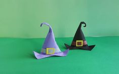 two paper witches sitting on top of a green surface with one wearing a black hat