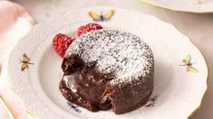 a piece of chocolate cake on a plate with raspberries and powdered sugar