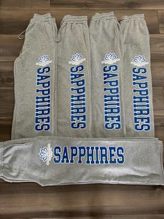 four gray sweatpants with blue and white logos on them sitting on a wooden floor