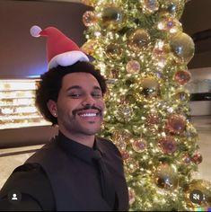 a man wearing a santa hat standing in front of a christmas tree