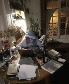 a person sitting at a table with books and papers on it, looking at a laptop