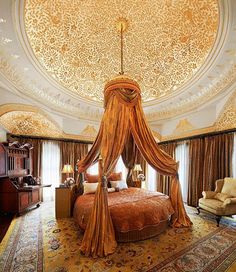 an elaborately decorated bed in a bedroom with gold drapes and curtains on the ceiling