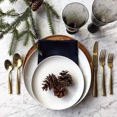 a place setting with pine cones, napkins and silverware on a marble table