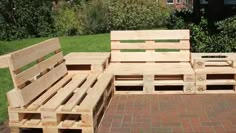 a wooden bench made out of pallets sitting on top of a brick floor next to a green field