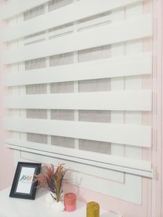 a white window covering with horizontal blinds in a pink room next to a framed photograph