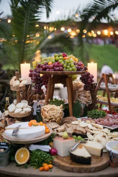 an assortment of cheeses, meats and fruits on a table with candles in the background