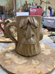 two mugs sitting on top of a table covered in clay, one with a face