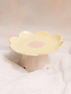 a yellow flower shaped plate sitting on top of a white cloth covered tablecloth,