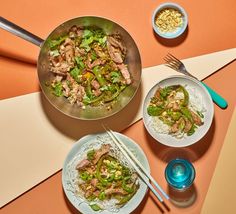 a table topped with two plates of food and chopsticks next to bowls of rice